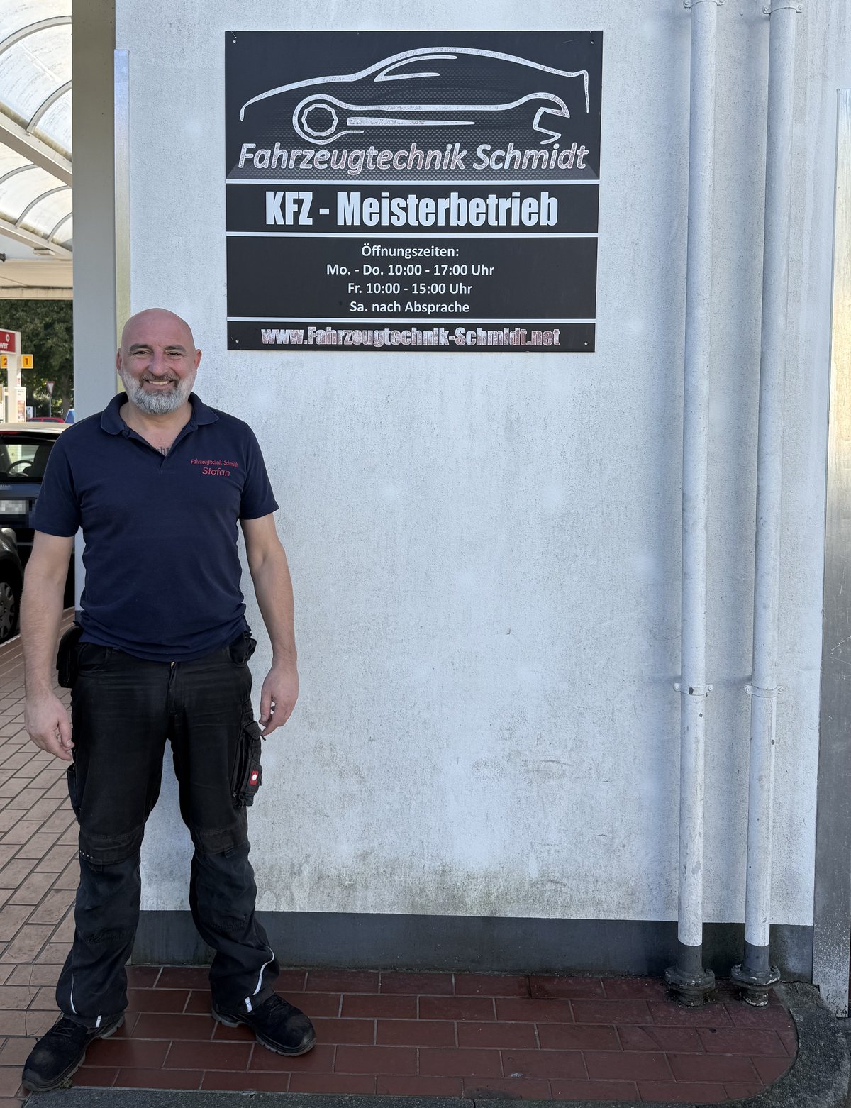 Stefan Schmidt, Kfz-Meister, lächelnd vor dem Schild seiner Werkstatt